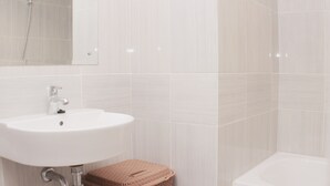 A bathroom with a white sink, a mirror, a shower, and a bathtub. - Minimalist And Cozy Studio At Vasanta Innopark Apartment (Cikarang)