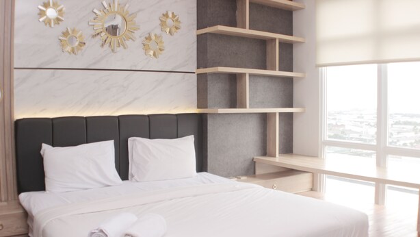A modern hotel room with a large bed, built-in shelving, and a city view. - Minimalist And Cozy Studio At Vasanta Innopark Apartment (Cikarang)