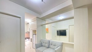 Ein modernes Wohnzimmer mit einem grauen Sofa, einem flachbildfernseher an der Wand und einem großen Spiegel, der den Raum reflektiert.