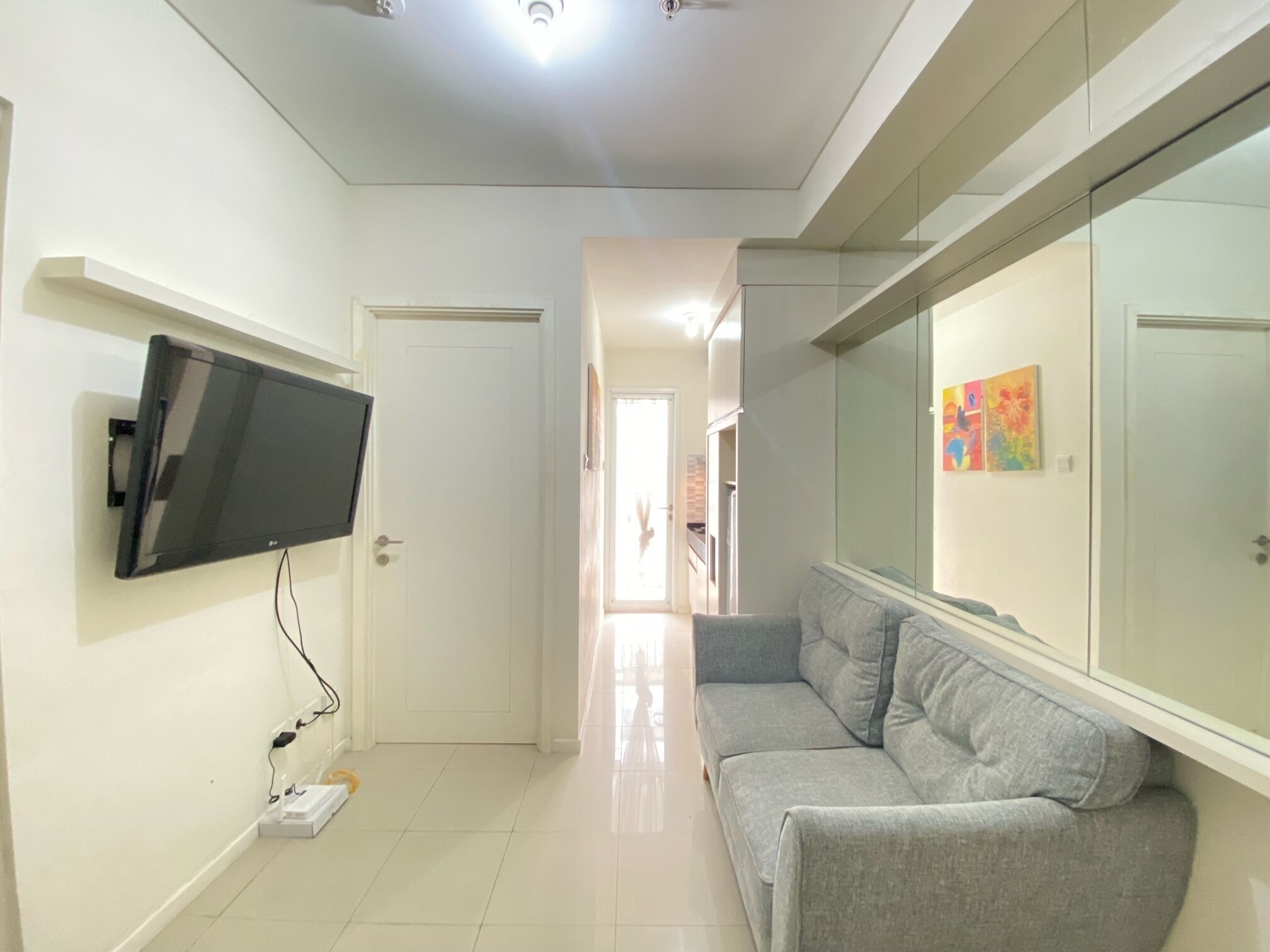 Una sala de estar moderna con un televisor de pantalla plana montado en la pared, un sofá gris y un aparador de vidrio con obras de arte.