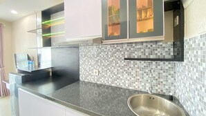 A modern kitchen with a granite countertop, stainless steel sink, and white cabinets. - Affordable Studio Room At Taman Melati Jatinangor Apartment (Hegarmanah)