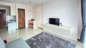 Un salon moderne doté d’un téléviseur à écran plat, d’un tapis gris et d’un coin cuisine avec un évier et des tabourets de bar rouges.