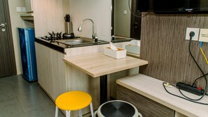 A compact kitchen with a sink, stove, and a small stool. - Minimalist And Comfy Studio At Bintaro Icon Apartment (South Tangerang)