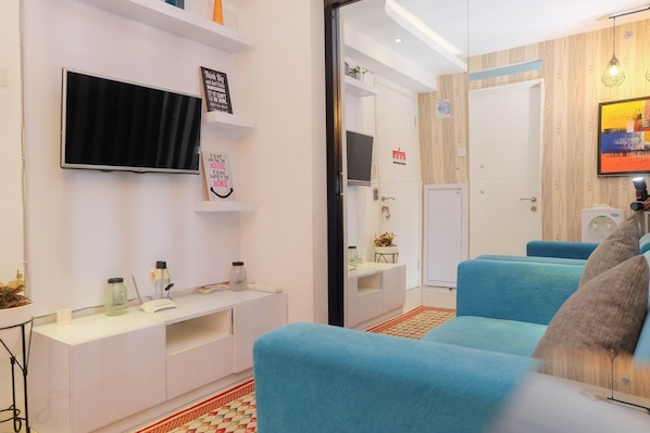 A modern living room with a flat-screen TV, white entertainment unit, and blue sofas.