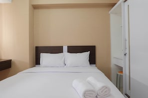 A neatly made bed with white linens and pillows, a wooden headboard, and a white wardrobe with a mirror.