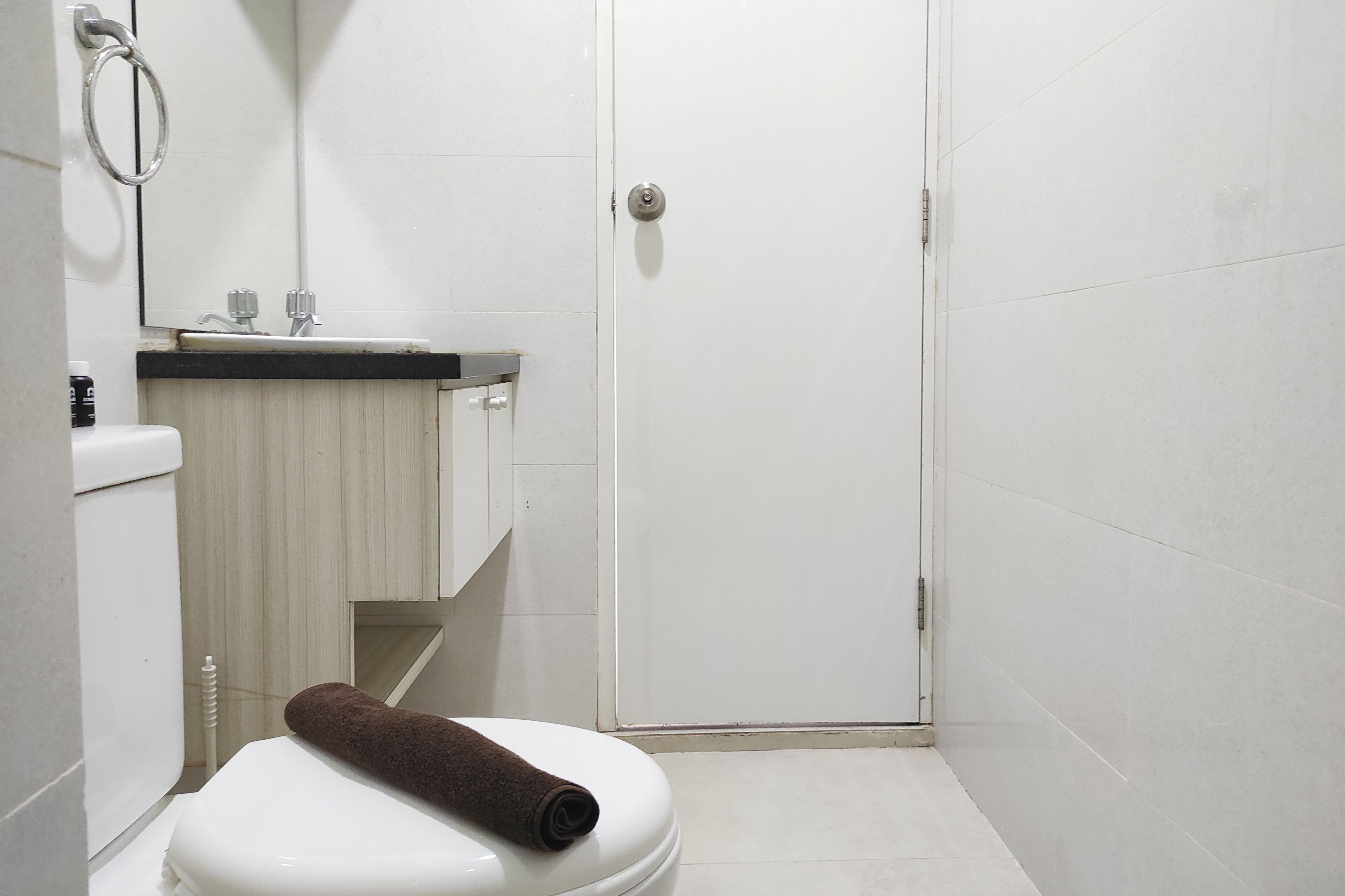 Une petite salle de bain propre, avec des toilettes, un lavabo et une serviette posée sur les toilettes.