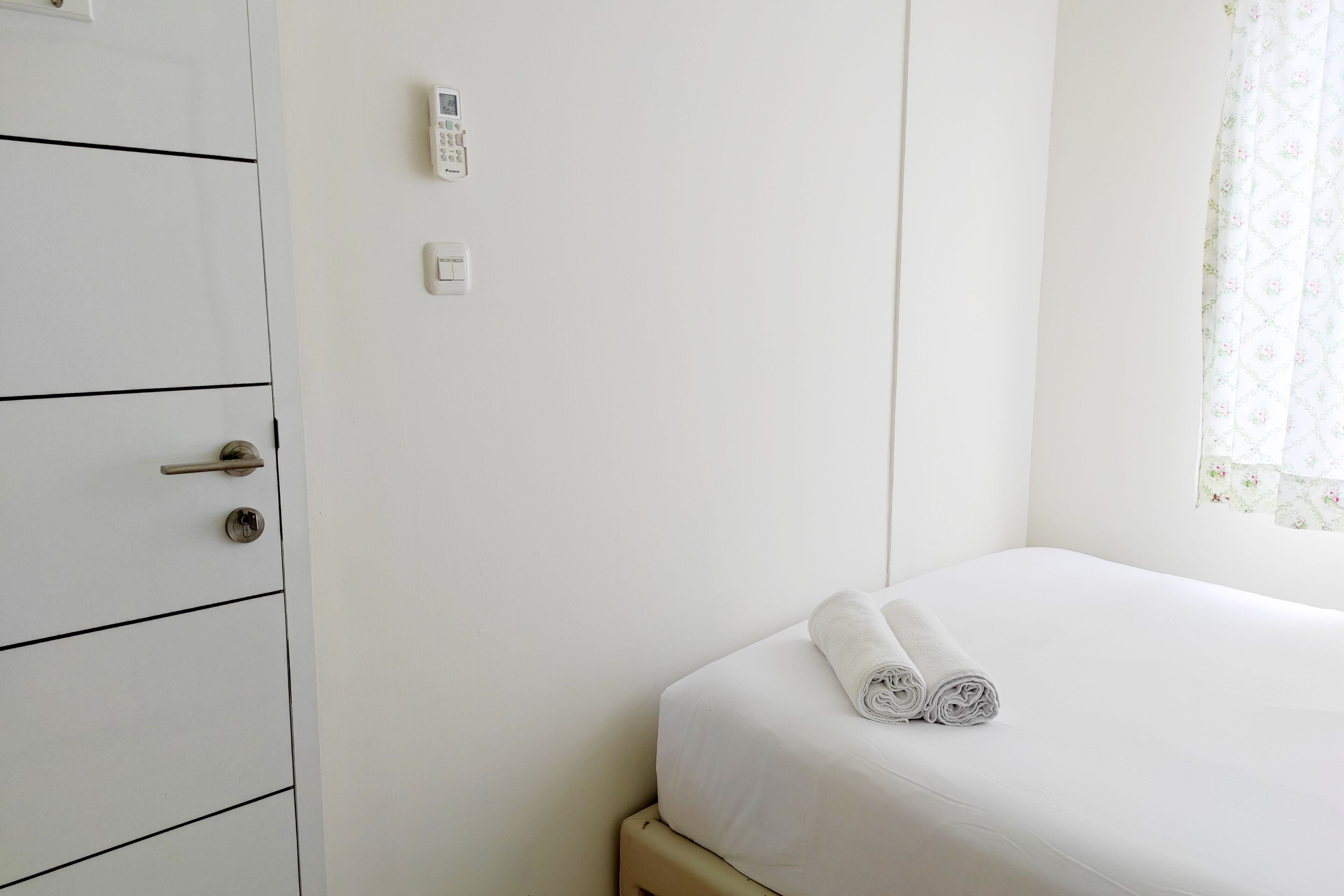 A hotel room with a bed, a wardrobe, and a thermostat on the wall.