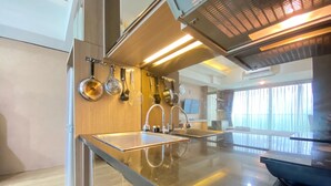 A modern kitchen with stainless steel appliances, a large island, and a view of the city. - Spacious Studio Room At Tamansari La Grande Apartment Near Bip (Bandung)