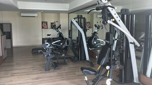 A gym with various exercise machines, wooden flooring, and a large mirror. - Spacious Studio Room At Tamansari La Grande Apartment Near Bip (Bandung)