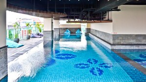 An indoor swimming pool with clear blue water, surrounded by tiled walls and a wooden deck. - Spacious Studio Room At Tamansari La Grande Apartment Near Bip (Bandung)