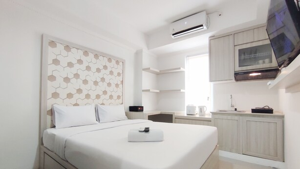 A modern hotel room with a neatly made bed, a small bedside table, a built-in TV, and a kitchen area with a microwave and a kettle. - Nice Cozy Studio At Paltrow City Apartment (Semarang)