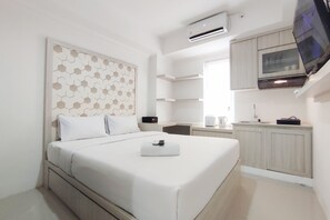 Ein modernes Hotelzimmer mit einem ordentlich bezogenen Bett, einem kleinen Nachttisch, einem integrierten Fernseher und einer Küchenzeile mit Mikrowelle und Wasserkocher.