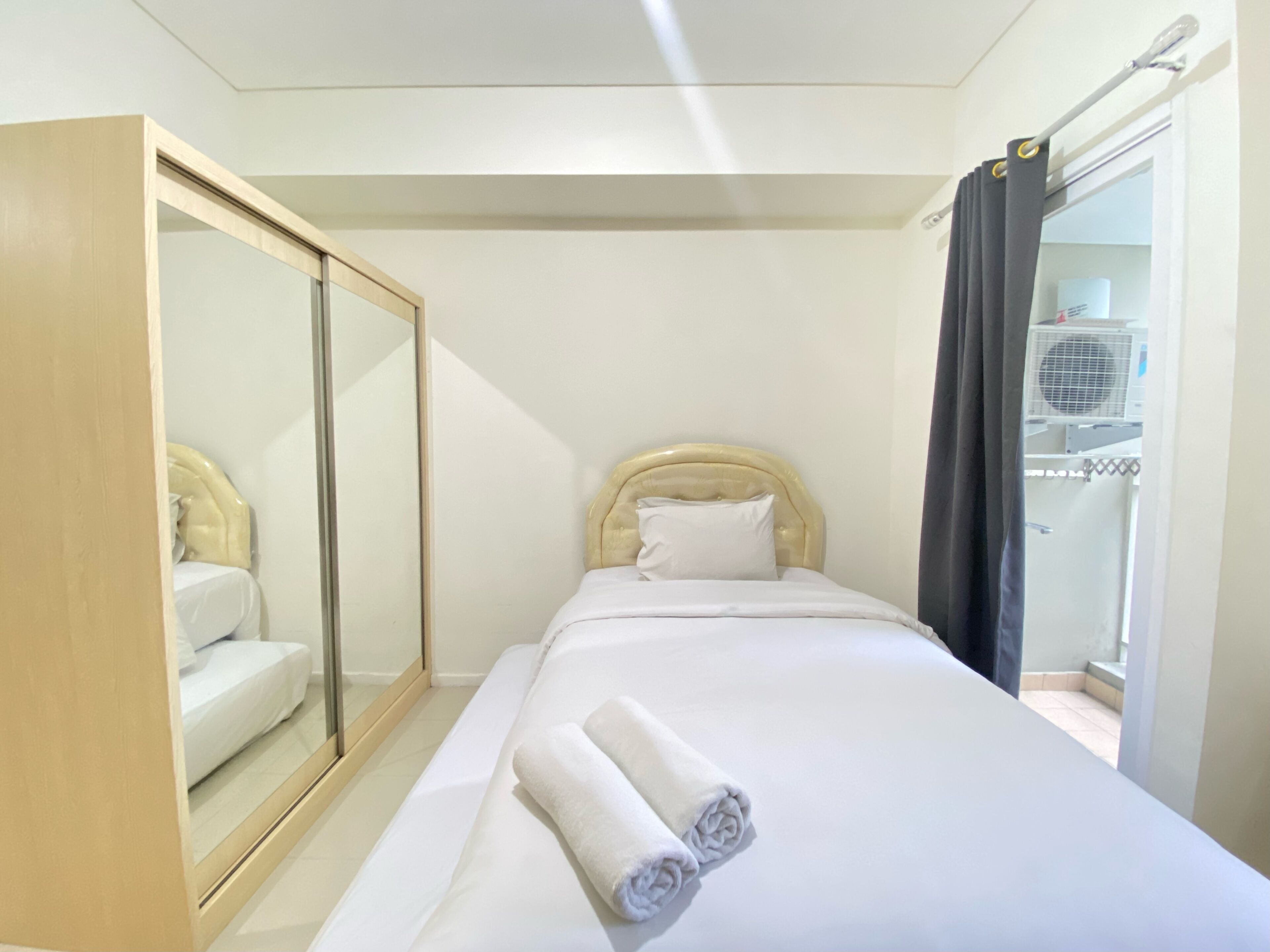 A hotel room with a bed, a mirror, a wardrobe, and a window.
