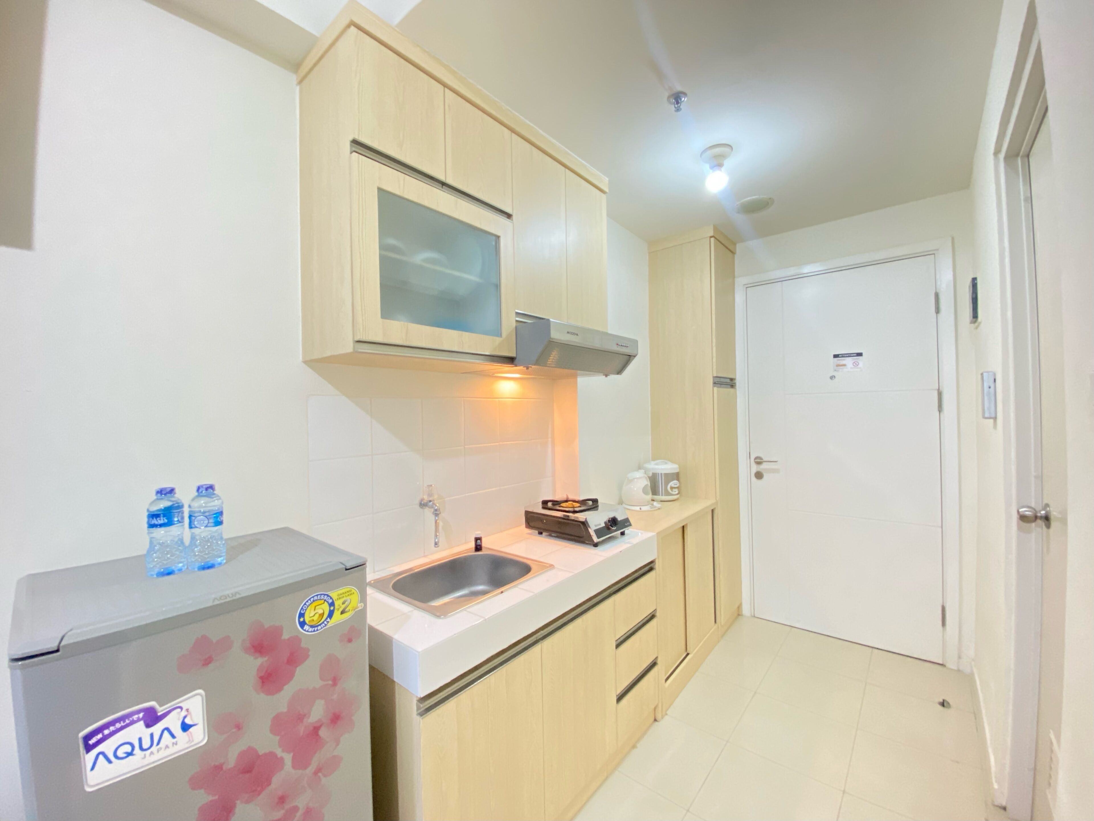 A compact kitchen with wooden cabinets, a stainless steel sink, and a refrigerator with a water bottle sticker.