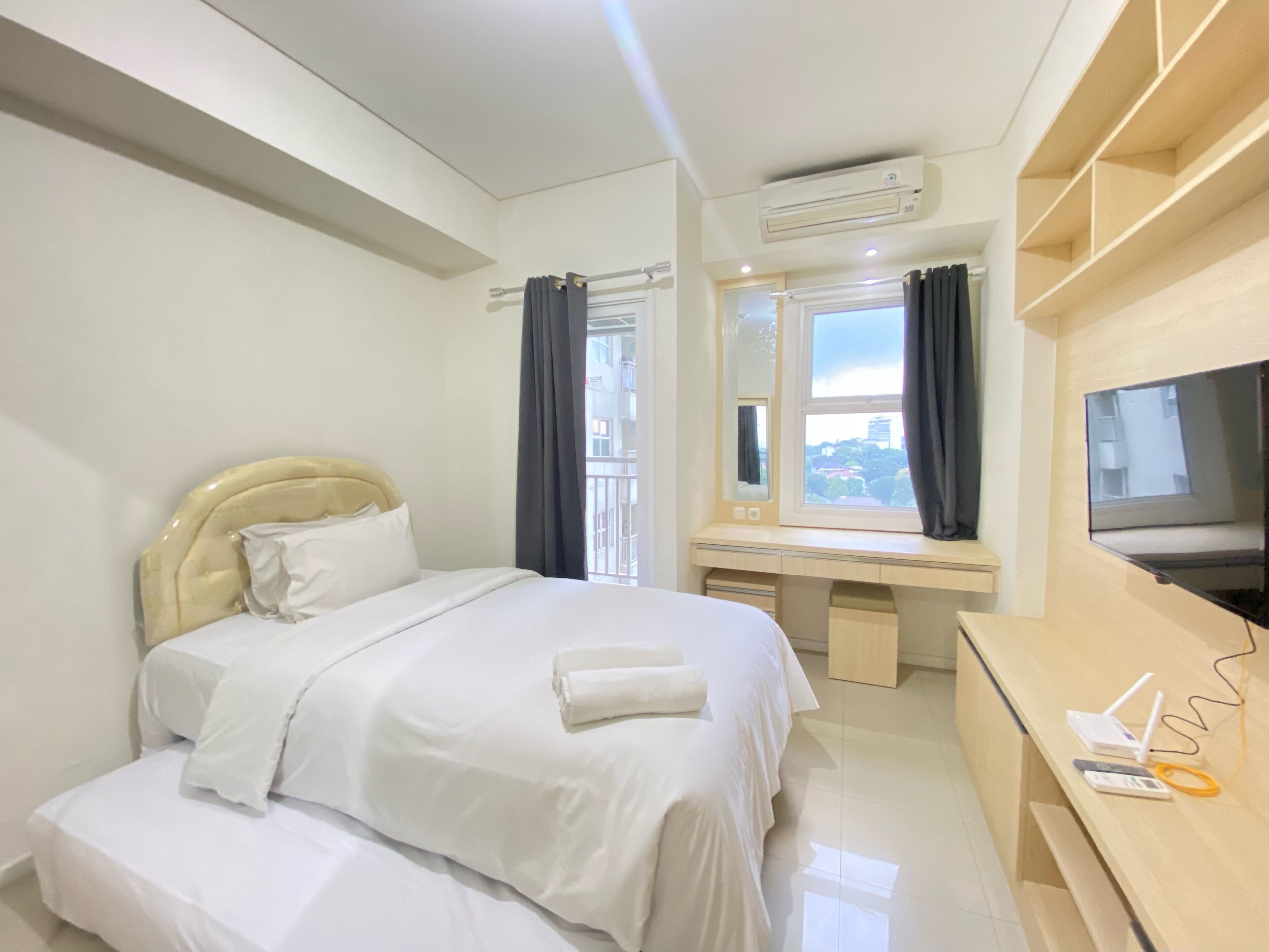 A modern hotel room with a bed, a desk with a flat-screen TV, and an air conditioning unit.