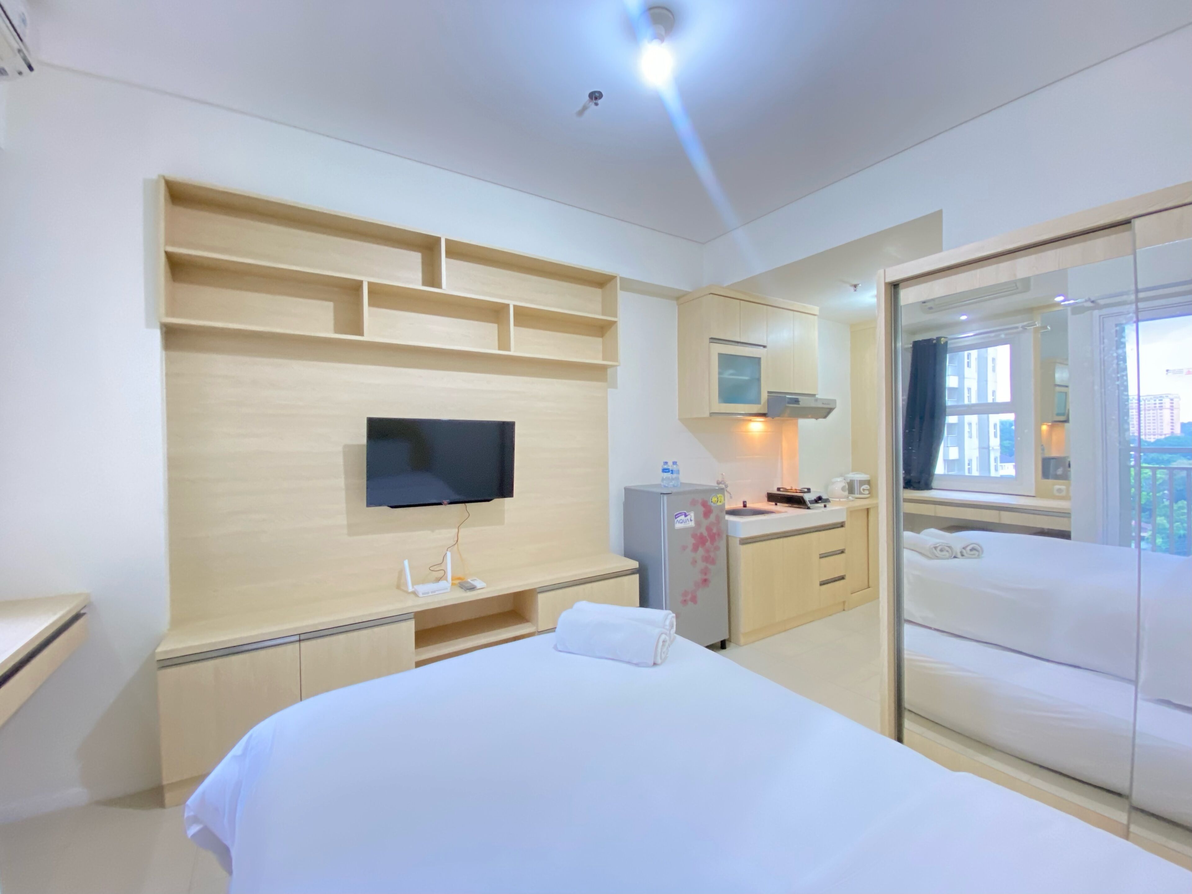 A hotel room with a bed, a TV mounted on the wall, a small kitchenette, and a balcony with a view.