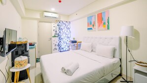 Hotelkamer met een bed, een televisie, een klein tafeltje met een waterkoker, een wandairconditioner en een raam met een geometrisch gordijn.