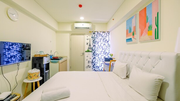 Een hotelkamer met een bed, een televisie, een waterautomaat, een klein tafeltje met een afstandsbediening en een wandklok.