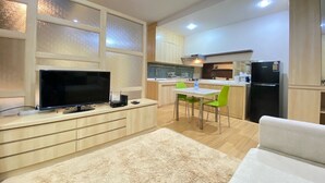 Eine moderne Küche mit Fernseher, ein Essbereich mit grünen Stühlen und ein weißes Sofa.