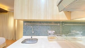 Ein modernes Badezimmer mit einem weißen Waschbecken, einer Glasdusche und einer gefliesten Rückwand.