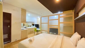 Ein modernes Hotelzimmer mit einem großen Bett, einer kleinen Küchenzeile und Blick auf den Küchenbereich.