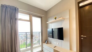 A modern living room with a large TV, sliding glass doors to a balcony, and a wooden console table. - Well Furnished And Private 2Br Mekarwangi Square Cibaduyut Apartment (Bandung)