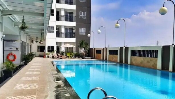 A swimming pool with a clear blue water, surrounded by a tiled deck and a building with balconies. - Well Furnished And Private 2Br Mekarwangi Square Cibaduyut Apartment (Bandung)
