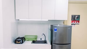 A compact kitchen with white cabinets, a stainless steel refrigerator, a sink, and a green basket. - Warm And Minimalist 3Br Apartment At M-Town Residence (Gading Serpong)