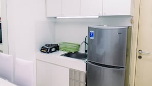 A kitchen with white cabinets, a stainless steel refrigerator, a green basket, and a black radio. - Warm And Minimalist 3Br Apartment At M-Town Residence (Gading Serpong)