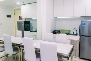 A modern kitchen with white cabinets, a stainless steel refrigerator, and a glass dining table with white chairs. - Warm And Minimalist 3Br Apartment At M-Town Residence (Gading Serpong)