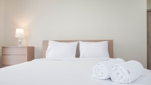 A neatly made bed with white linens and two rolled towels, a bedside lamp, and a wooden nightstand. - Nice And Comfort 2Br At Pejaten Park Apartment (Jakarta)