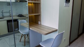 A compact kitchen with a wooden countertop, two white chairs, and a small TV. - Studio With Cozy Design At Sky House Bsd Apartment (Pagedangan)
