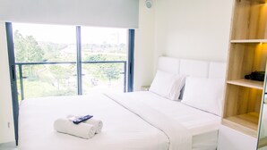 A modern hotel room with a large bed, a view of the city, and a wooden nightstand. - Studio With Cozy Design At Sky House Bsd Apartment (Pagedangan)