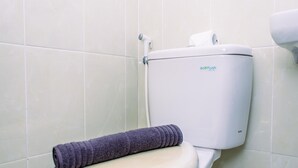 Sanitário com assento branco e uma toalha enrolada.