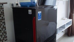 Uma cozinha compacta com geladeira, micro-ondas e um laptop em cima.