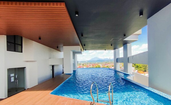 An indoor swimming pool with a view of a cityscape and mountains in the distance. - Cozy Living Studio At The Alton Apartment (Semarang)
