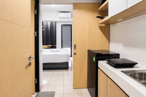 A compact kitchenette with a built-in stove, a sink, and a bed in the background. - Cozy Living Studio At The Alton Apartment (Semarang)