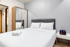 A hotel room with a bed, a mirror, a nightstand with bottled water, and a wooden wardrobe. - Cozy Living Studio At The Alton Apartment (Semarang)