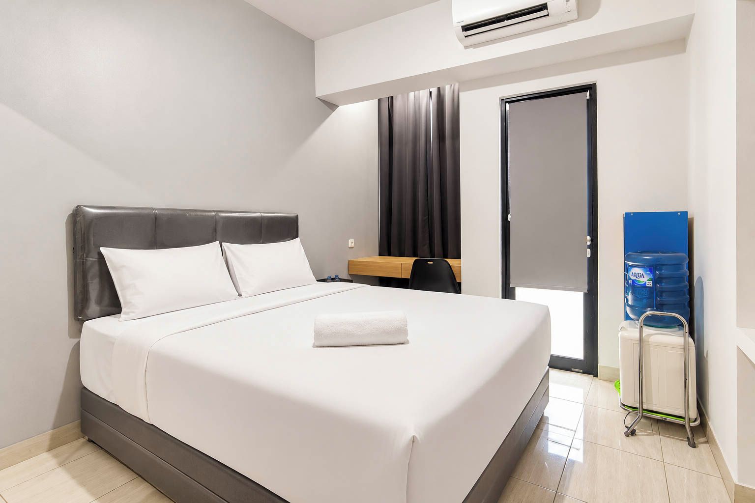 A modern hotel room with a bed, a bedside table, a water dispenser, and a door.