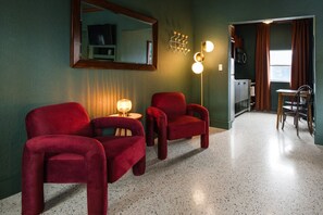 Une pièce avec deux chaises rouges, une petite table, un miroir et un luminaire fixé au mur.