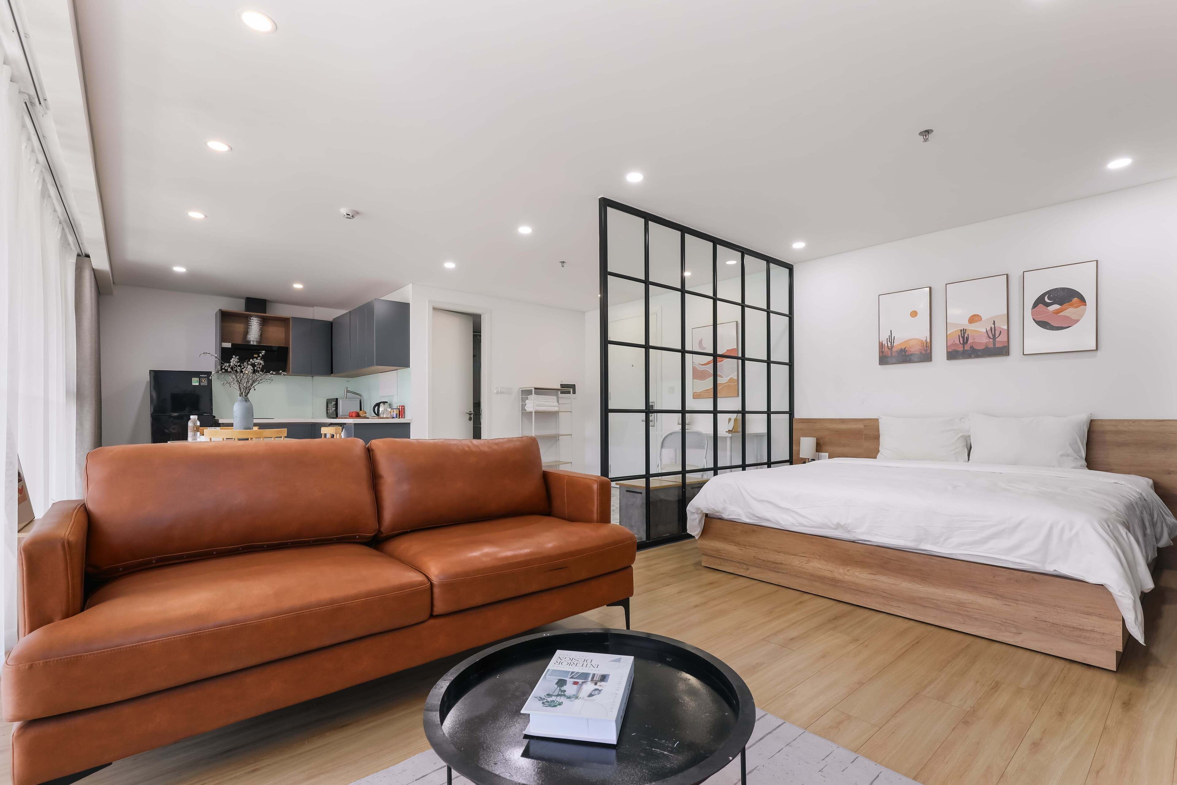 Habitación de hotel moderna con sofá de cuero, una mesa redonda negra, cama de madera y separador de vidrio.
