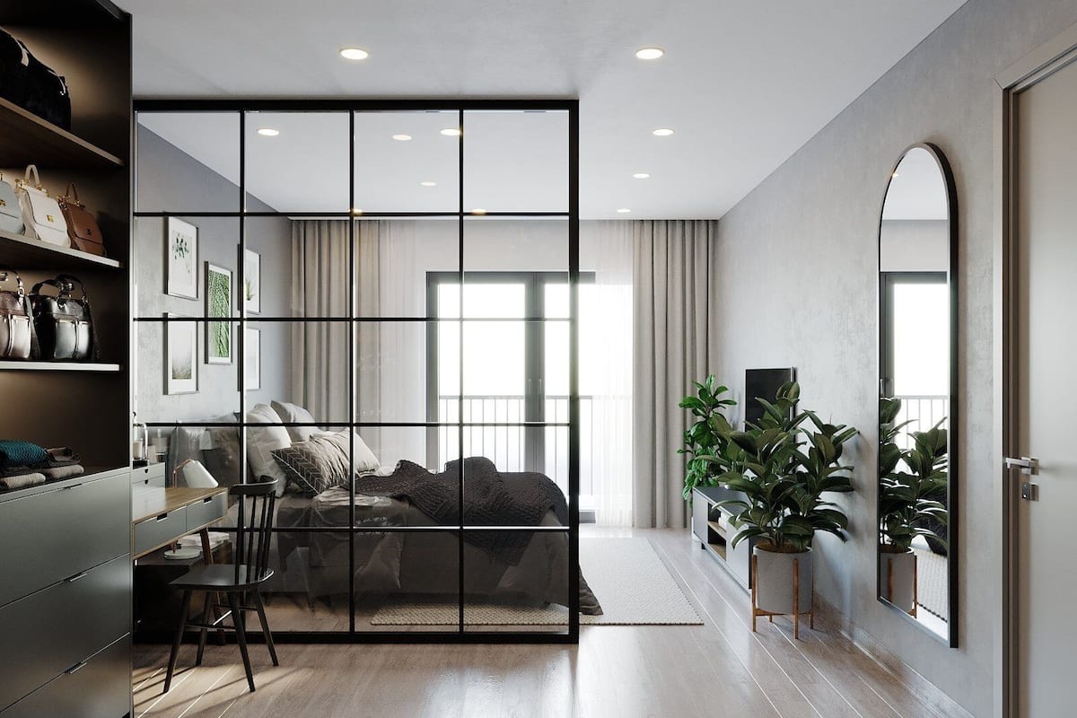 Quarto moderno com uma cama grande, uma escrivaninha e uma cadeira. Há plantas e um espelho na parede.