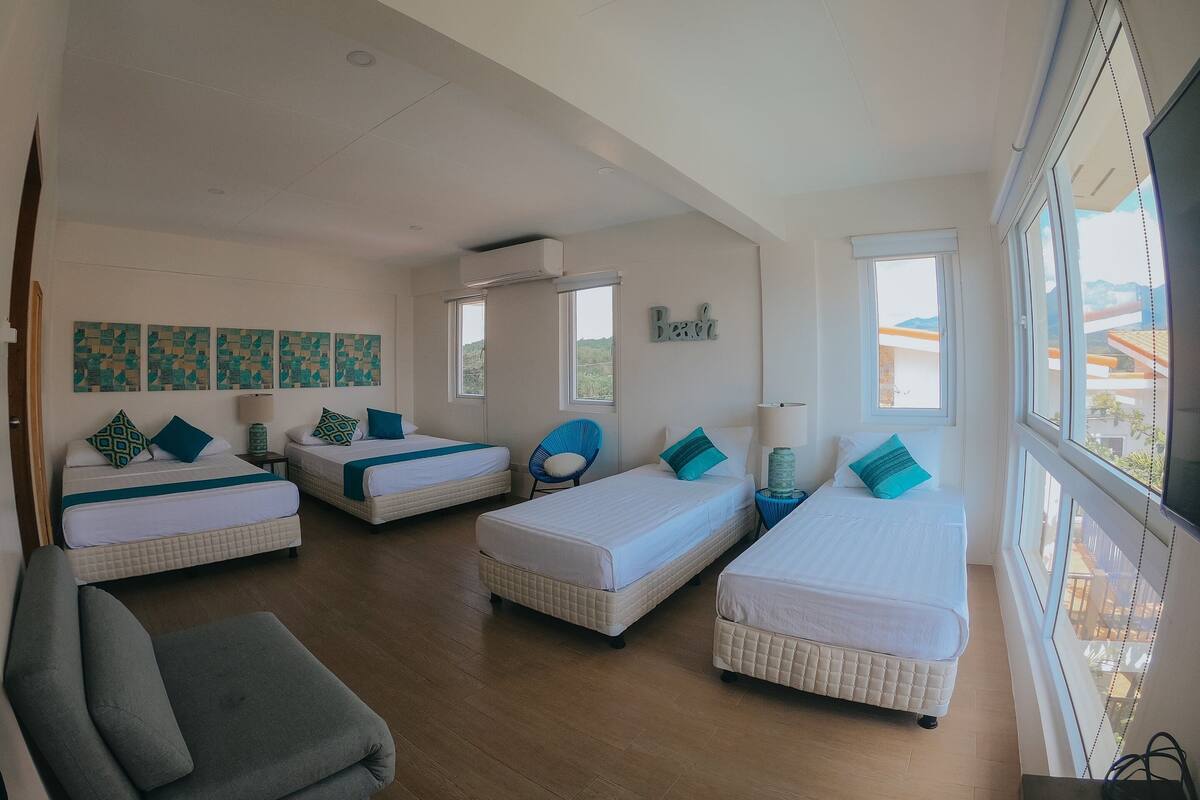 A hotel room with three beds, a sofa, and artwork on the walls.