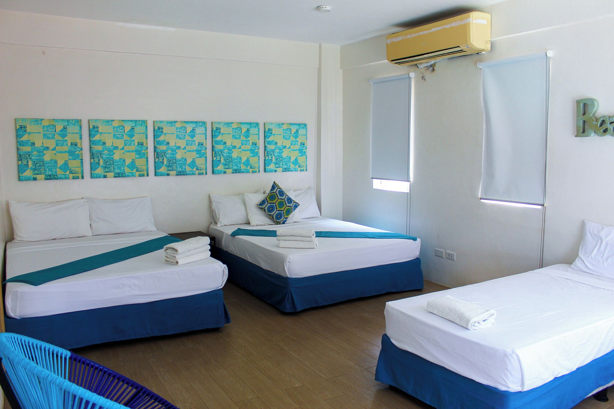 Habitación de hotel con dos camas, una ventana y una pared decorada con cuatro obras de arte azules y amarillas.