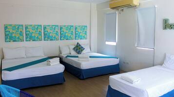 Habitación de hotel con dos camas, una ventana y una pared decorada con cuatro obras de arte azules y amarillas.