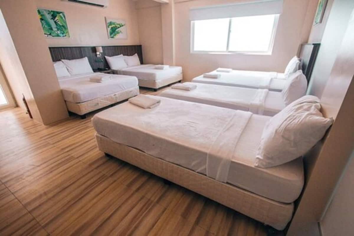 A hotel room with two single beds, a large bed, and a window providing natural light.