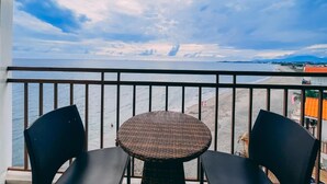 Un balcon avec une table en osier et deux chaises, donnant sur une plage et l’océan.