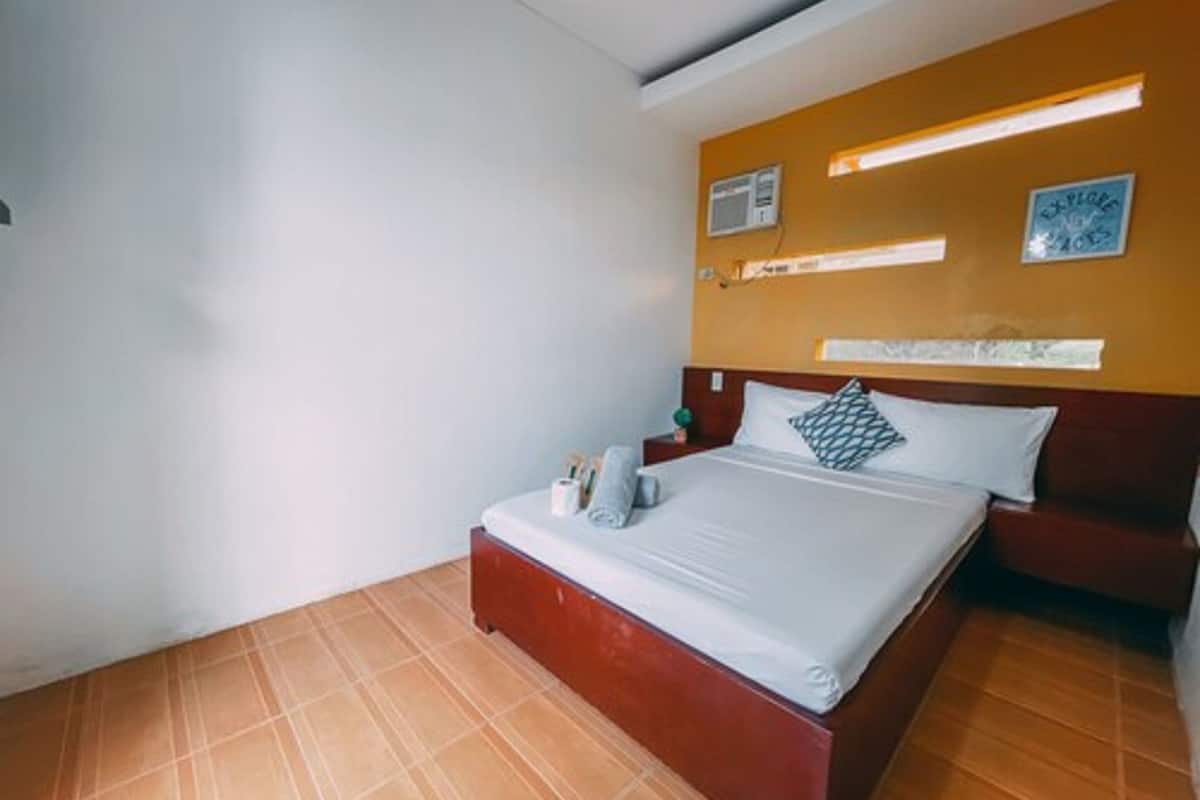 A hotel room with a bed, a nightstand, and a wall-mounted air conditioner.