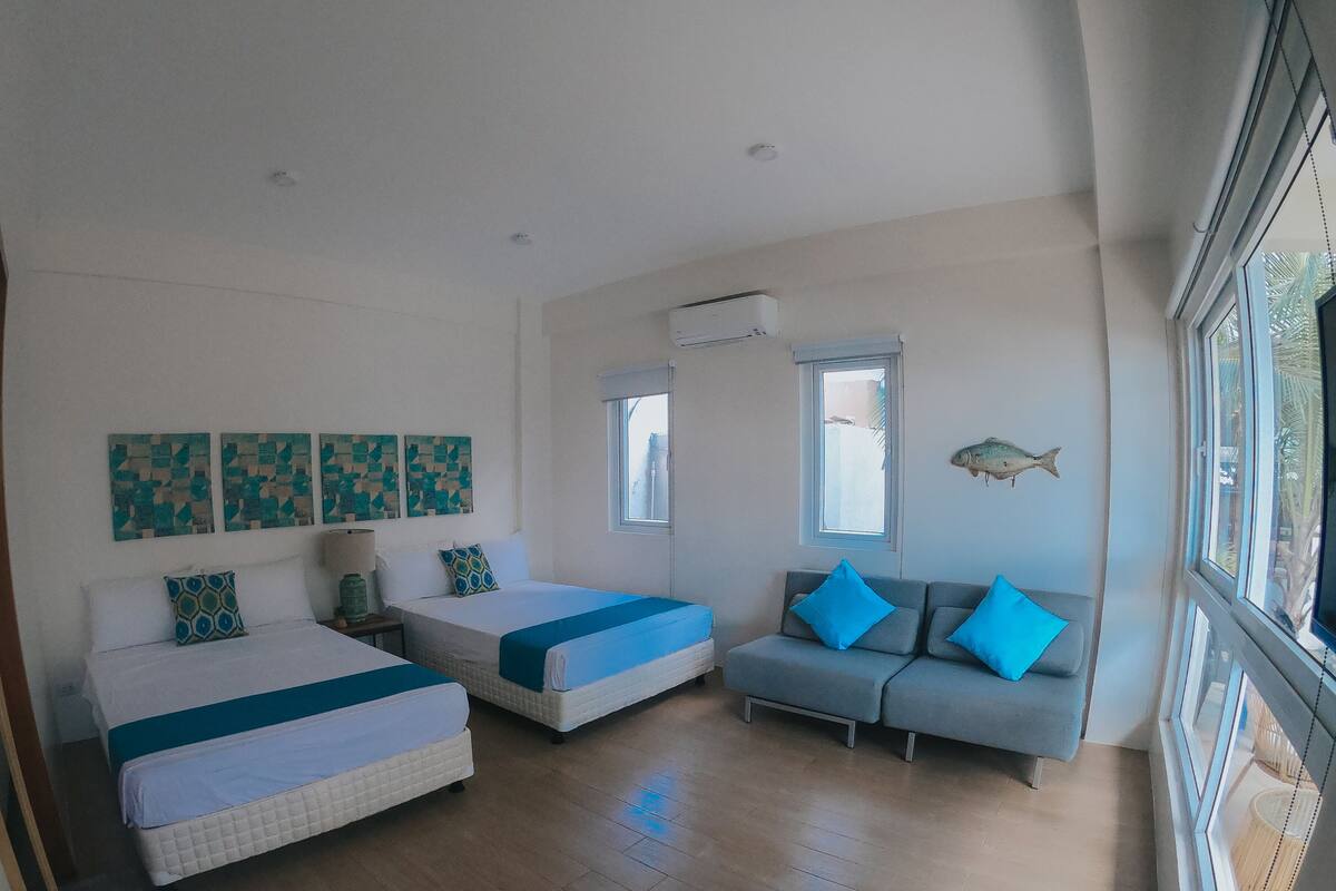 A room with two beds, a sofa, and a window with a view.