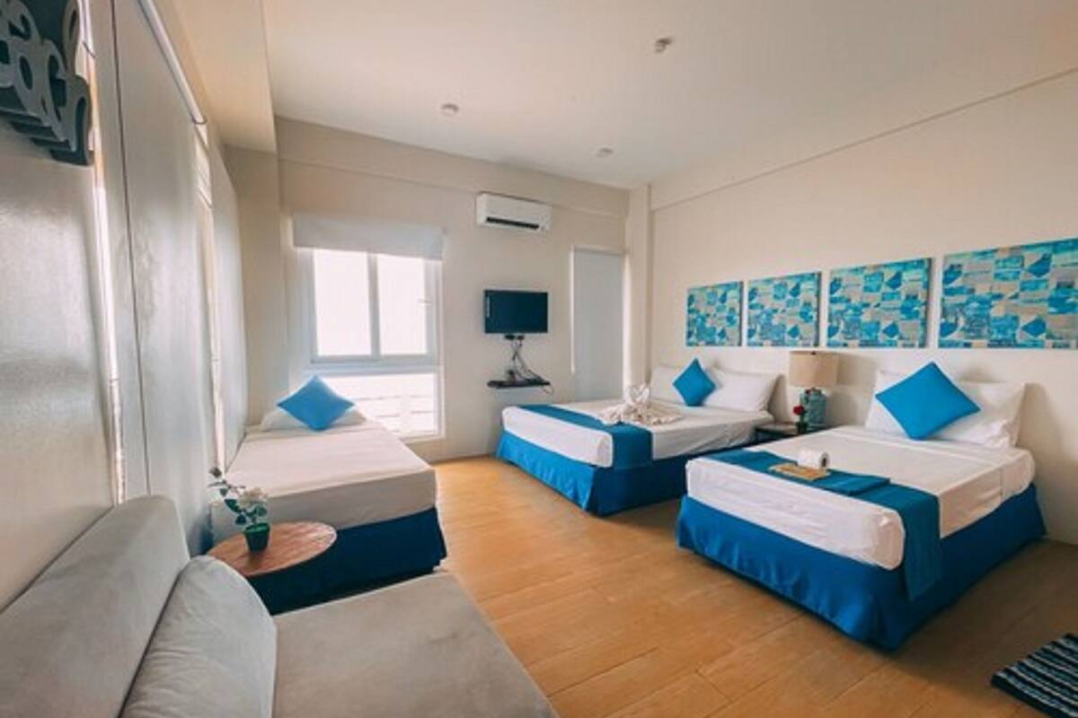 A hotel room with two beds, a sofa, a TV, and artwork on the wall.